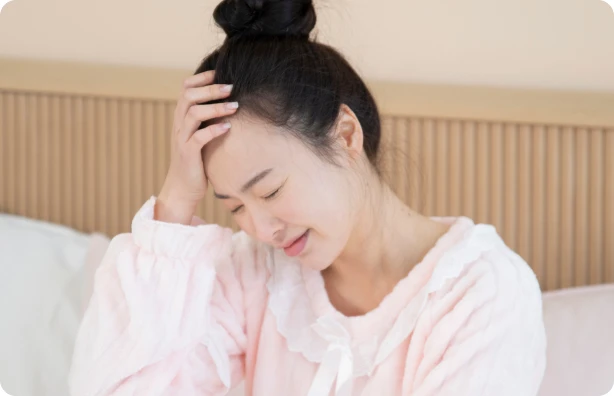 침대에 앉아 머리를 짚으며 힘들어하는 여성