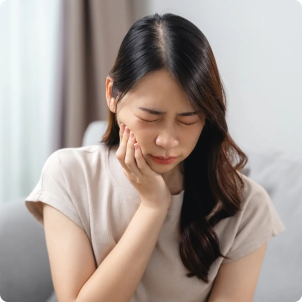 소파에 앉아 볼을 감싸 쥐고 통증을 참는 여성