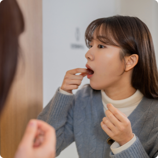 거울을 보며 입안의 혀를 손가락으로 확인하는 젊은 여성