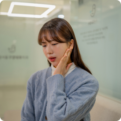 젊은 여성이 뺨에 손을 대고 입안의 불편감을 호소하는 표정을 짓는다.